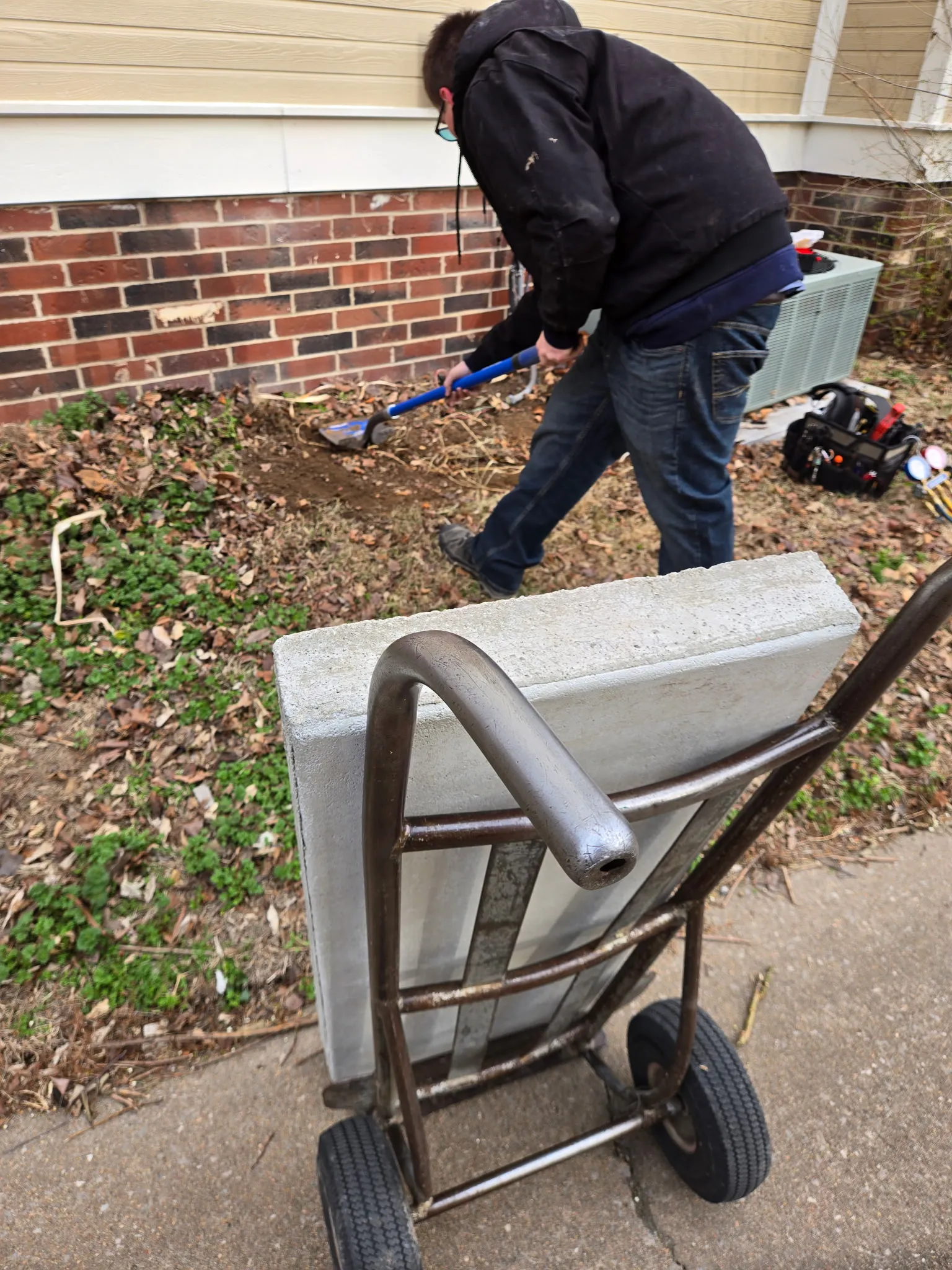 Technician leveling the ground to set a pad for a new AC condenser installation