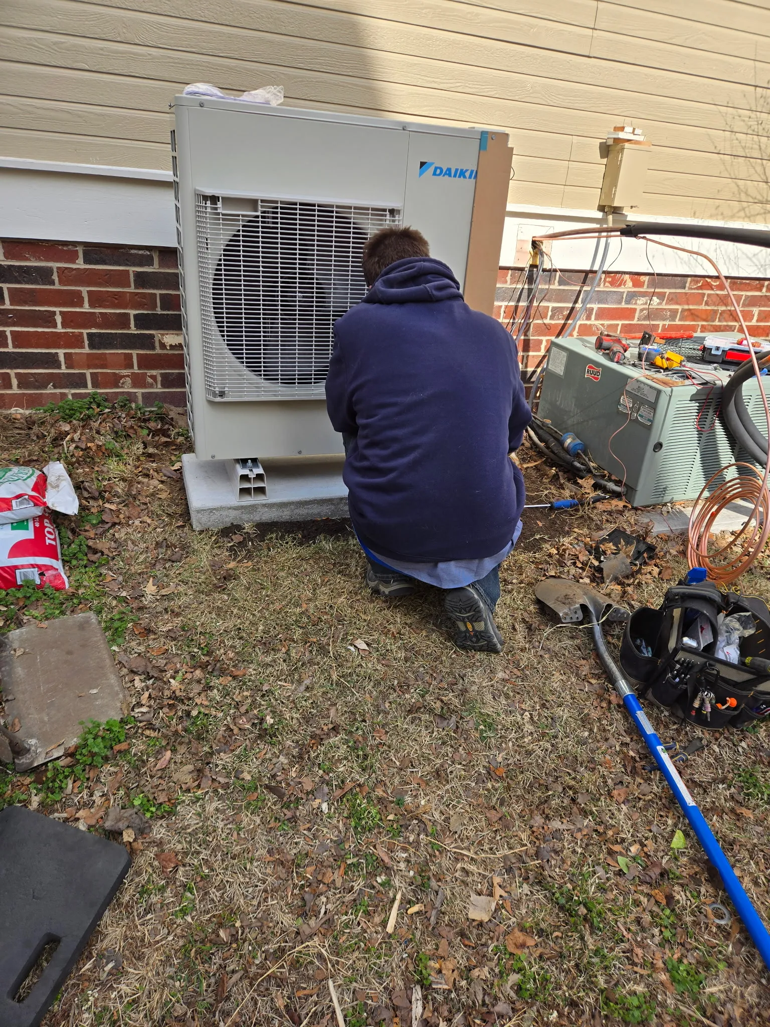 Technician connecting a newly installed heat pump condenser at a brick home