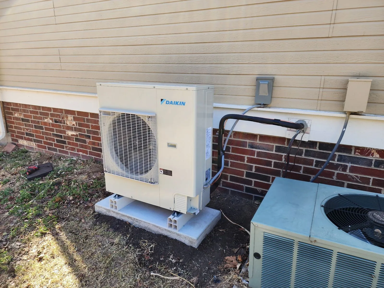New outdoor heat pump installed on a composite pad next to an older condenser