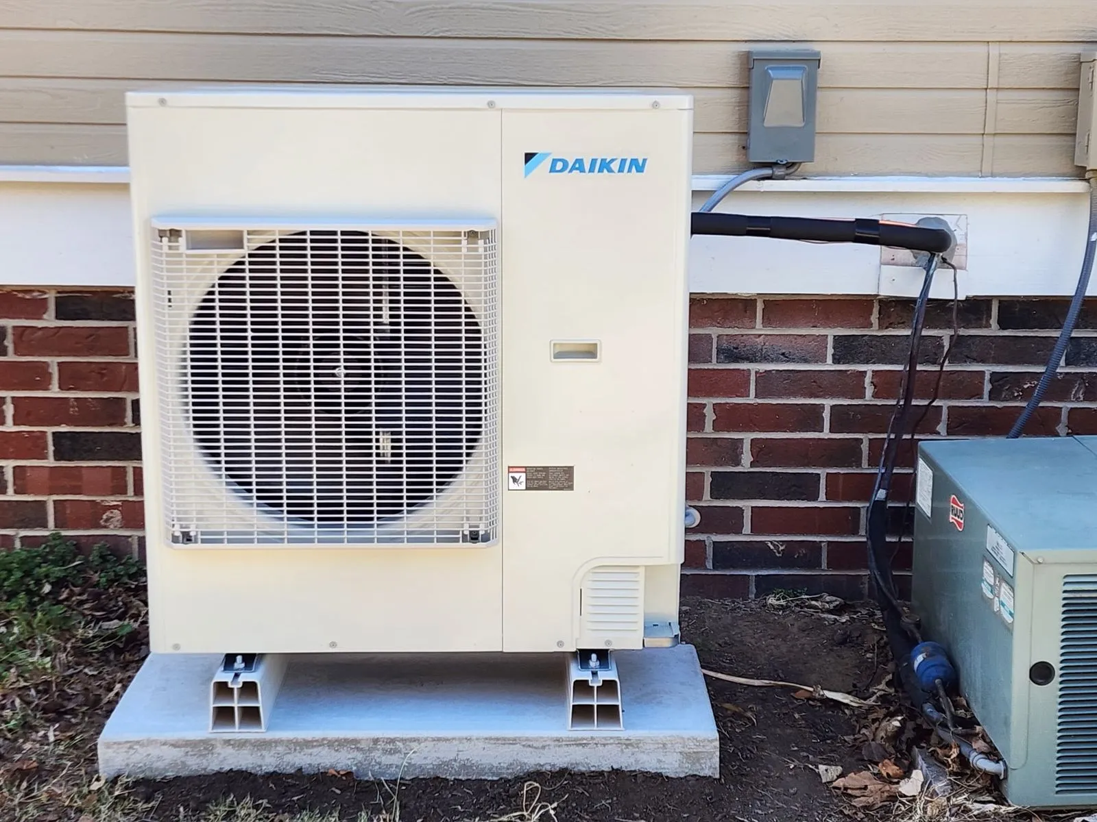 Completed heat pump installation on a concrete pad beside a brick home